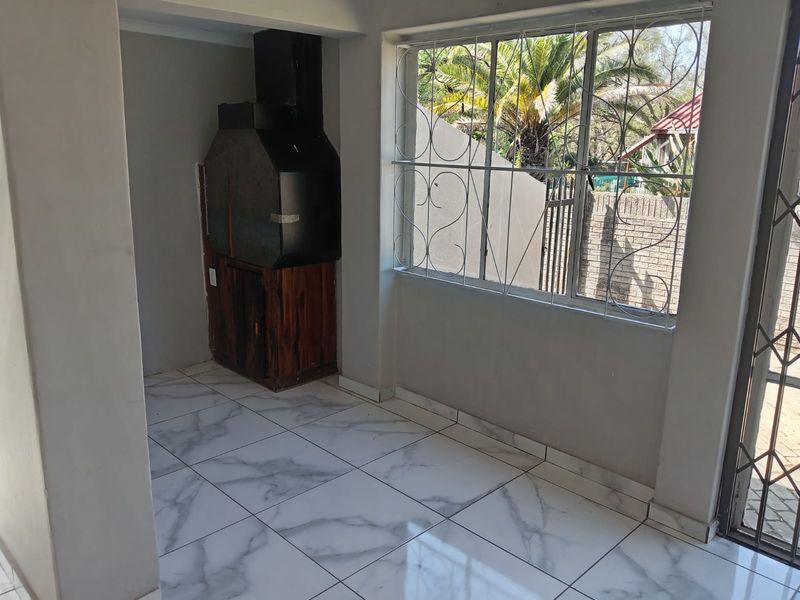 Covered patio area featuring a built-in braai, modern marble-look floor tiles, and secure window bars overlooking the garden.