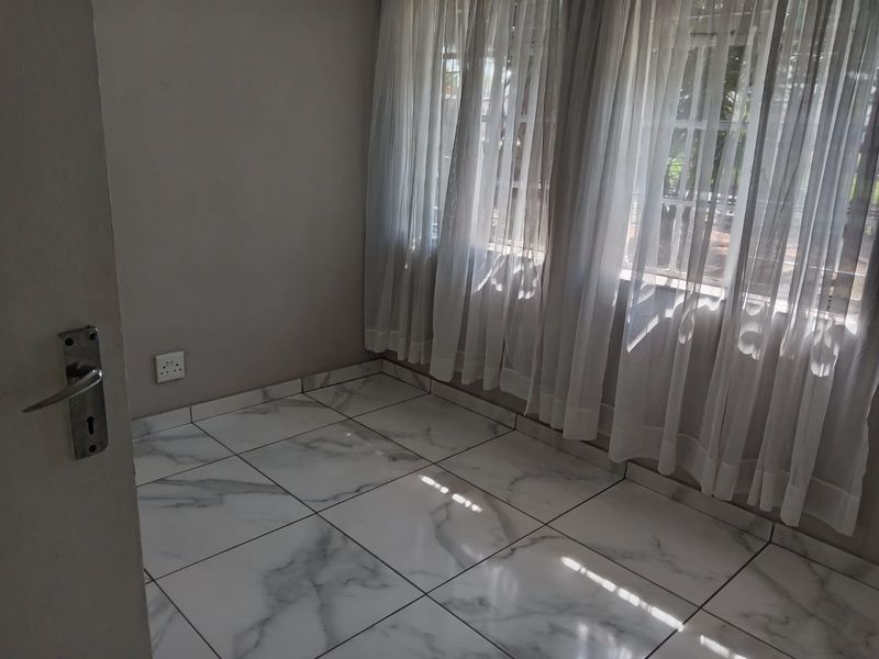 A bright, empty bedroom featuring modern marble-look floor tiles and large windows with sheer curtains, providing a clean and neutral space.