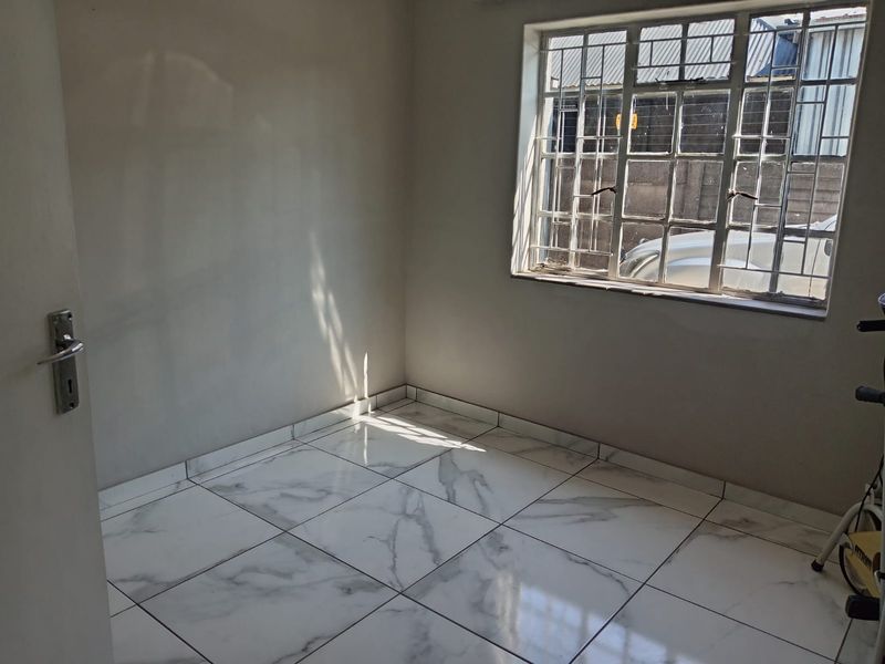 A bright, empty bedroom featuring modern marble-look floor tiles and a window fitted with security bars.