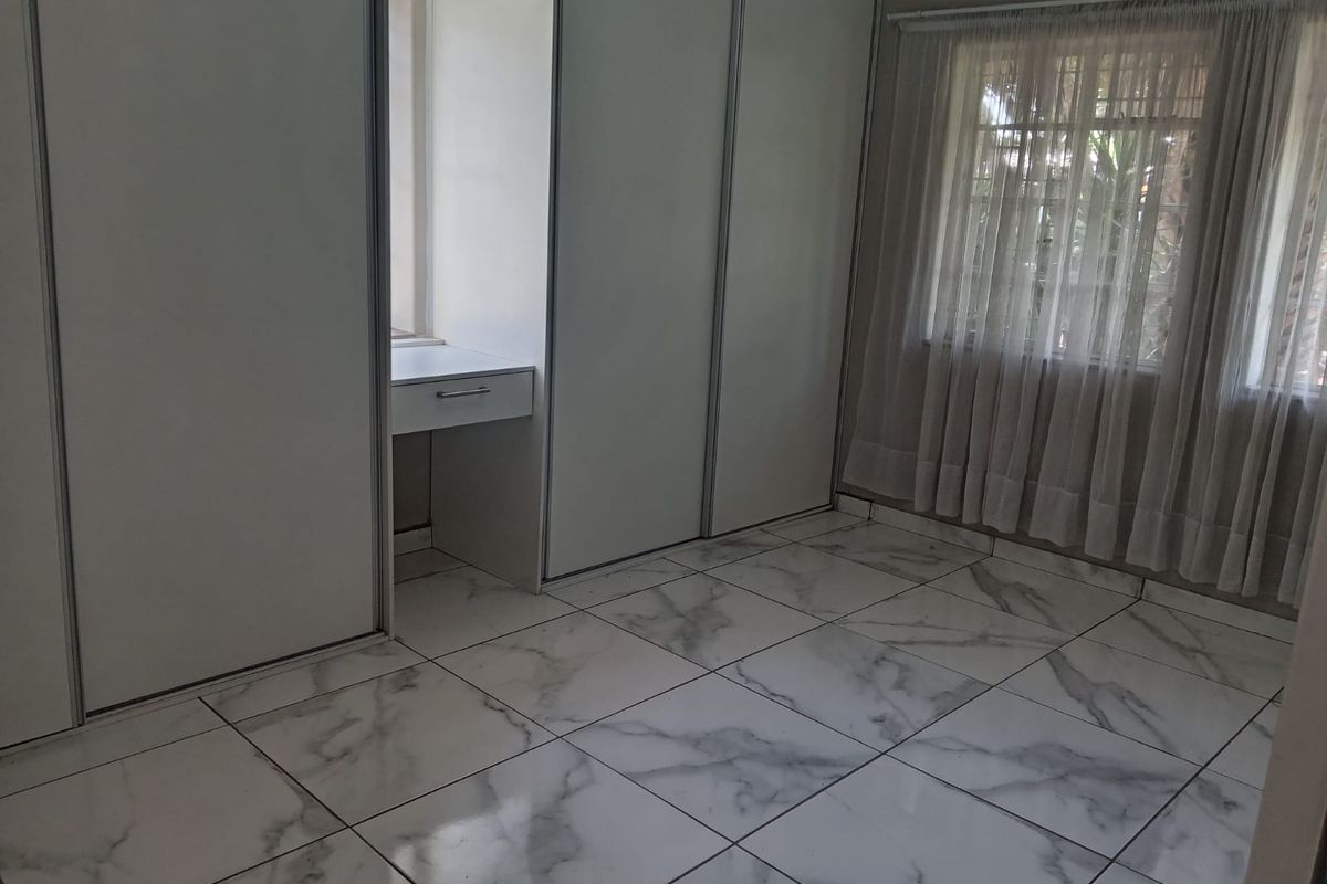 A bright, empty bedroom featuring modern marble-look floor tiles, extensive built-in cupboards, and a convenient integrated vanity area.