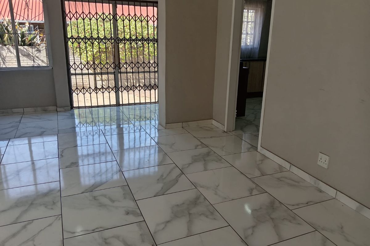 A bright, empty living area featuring modern marble-look floor tiles, a secure sliding glass door, and neutral wall finishes.