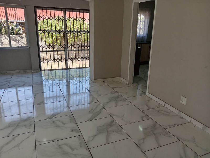 A bright, empty living area featuring modern marble-look floor tiles, a secure sliding glass door, and neutral wall finishes.