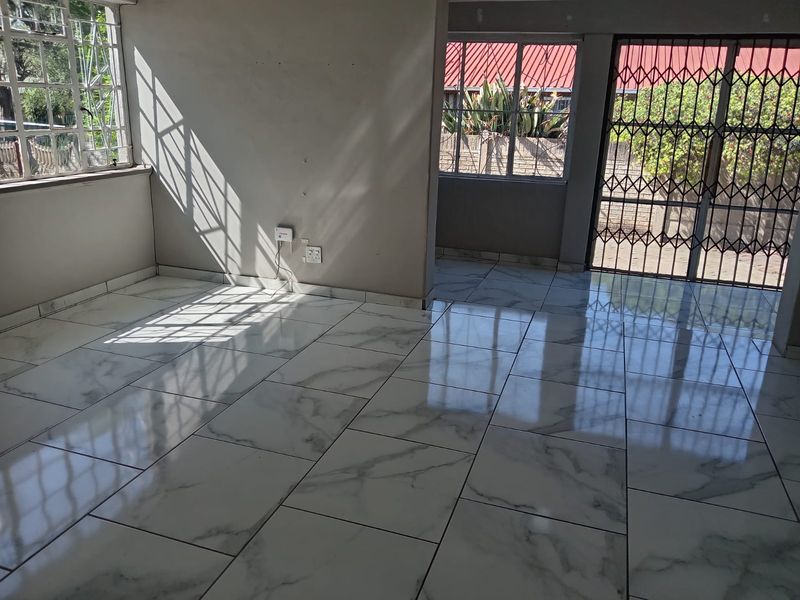 A bright, vacant living area featuring polished marble-look floor tiles, secure window bars, and a security gate leading to the exterior.