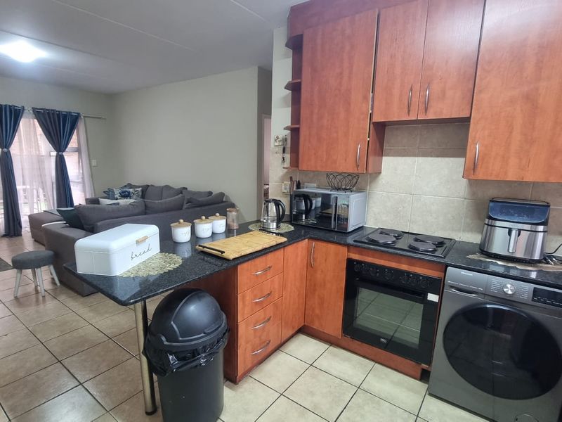 Open-plan kitchen and living area featuring wooden cabinetry, granite countertops, built-in oven, and tiled flooring with direct access to an outdoor patio.