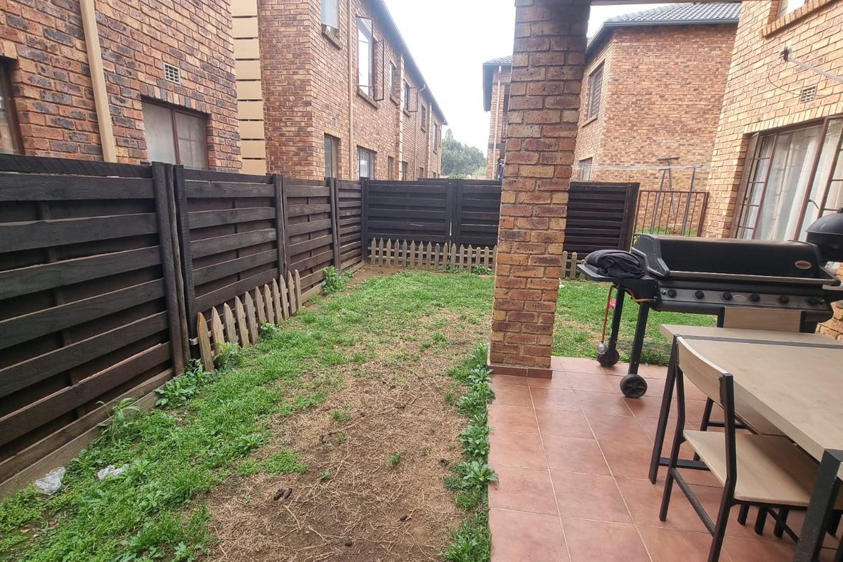 A private rear courtyard featuring a covered tiled patio area, brick pillar, and a small garden space enclosed by timber fencing.