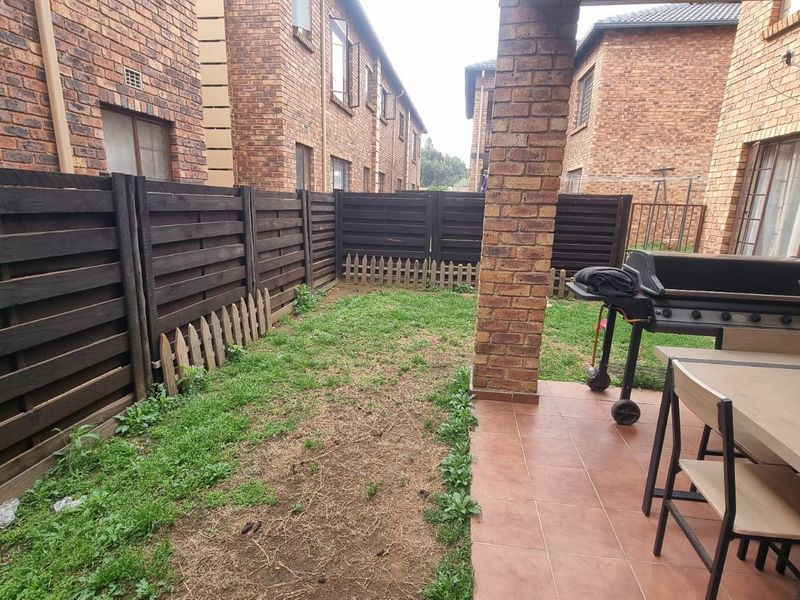 A private rear courtyard featuring a covered tiled patio area, brick pillar, and a small garden space enclosed by timber fencing.