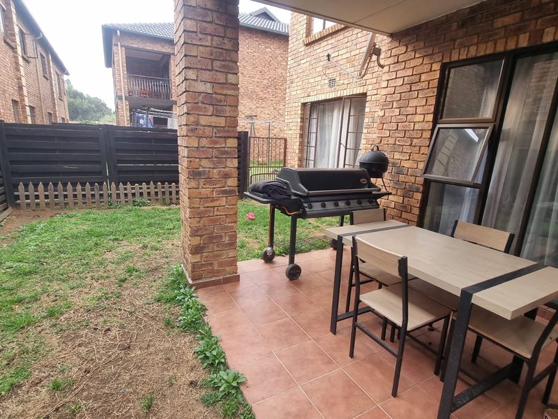 Covered patio area with tiled flooring and brick pillar, leading out to a small private garden with perimeter fencing.