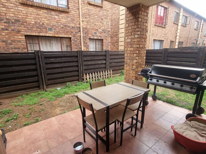 A covered patio area featuring tiled flooring and a brick support pillar, overlooking a private garden space with timber fencing.