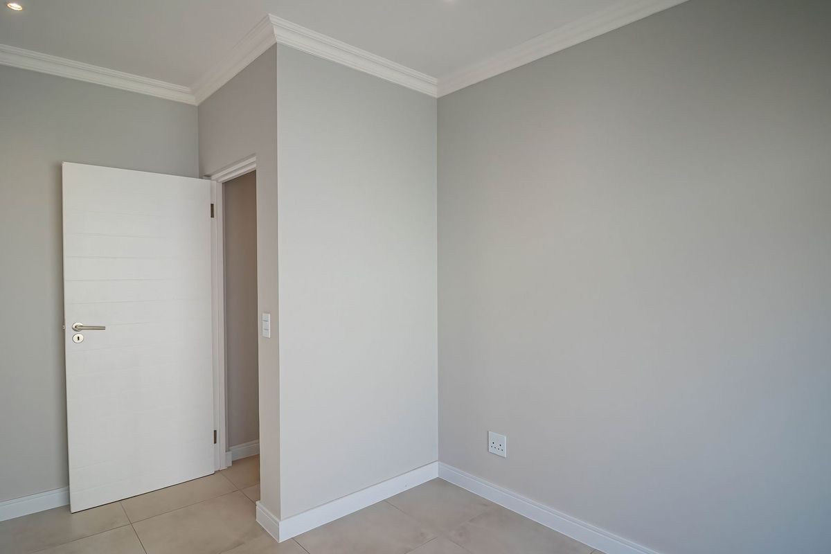 A clean, empty bedroom featuring neutral grey walls, crown molding, tiled flooring, and recessed lighting, providing a blank canvas for personalization.