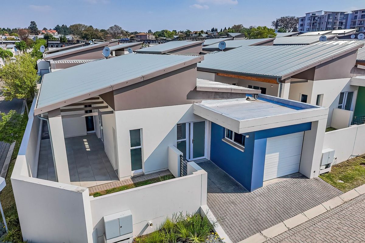 Aerial view of a modern townhouse featuring a metal roof, paved driveway, single garage, and a covered patio area within a residential complex.