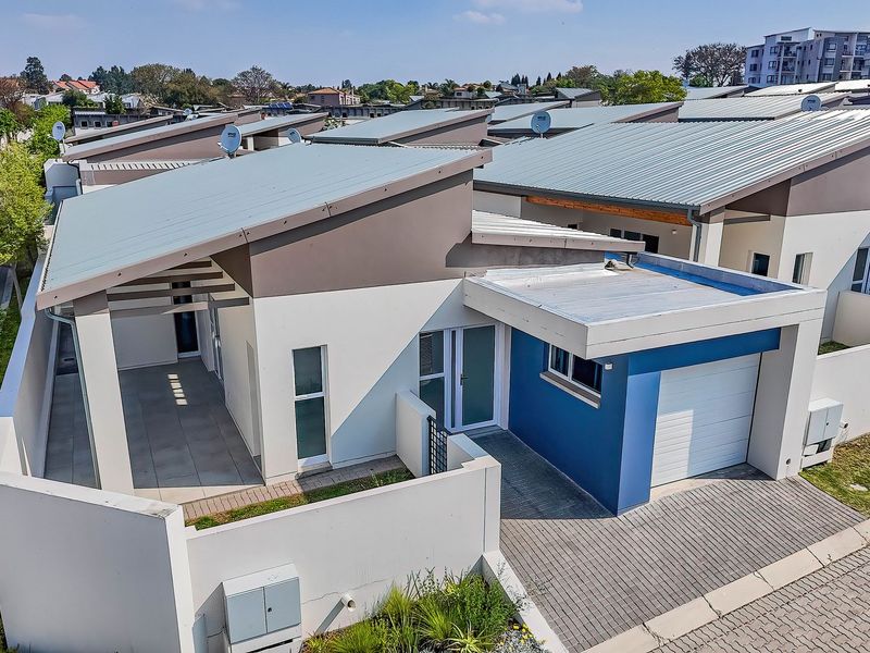 Aerial view of a modern townhouse featuring a metal roof, paved driveway, single garage, and a covered patio area within a residential complex.