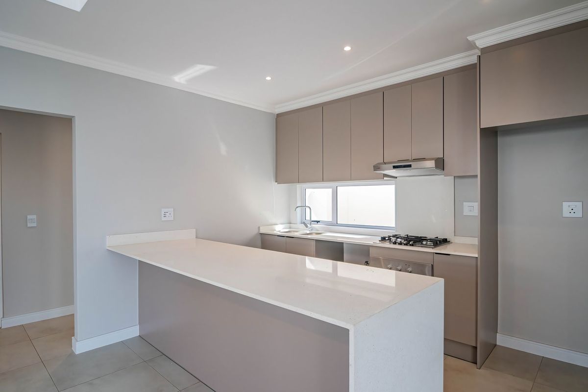 Modern kitchen featuring sleek taupe cabinetry, quartz countertops, a breakfast bar, gas hob, and integrated extractor fan, finished with neutral tiled flooring.