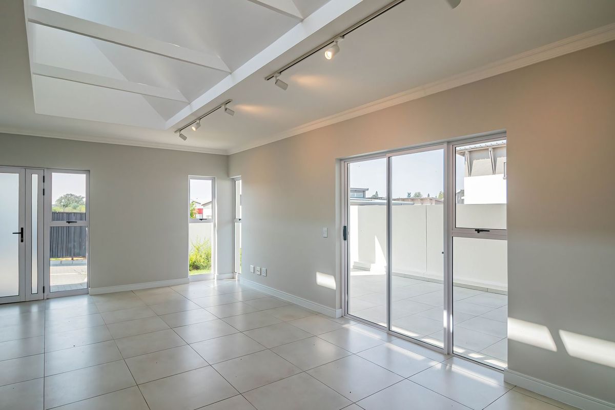 Spacious, light-filled living area featuring vaulted ceilings with skylights, modern track lighting, neutral tiled flooring, and direct access to an outdoor patio.