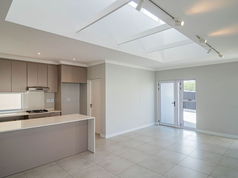 Modern open-plan kitchen and living area featuring a large skylight, neutral cabinetry, stone countertops, gas hob, and tiled flooring with direct access to the exterior.