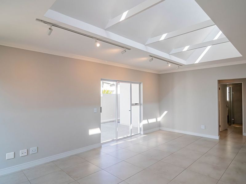 Spacious open-plan living area featuring large skylights, modern tiled flooring, and sliding glass doors leading to an outdoor patio space.