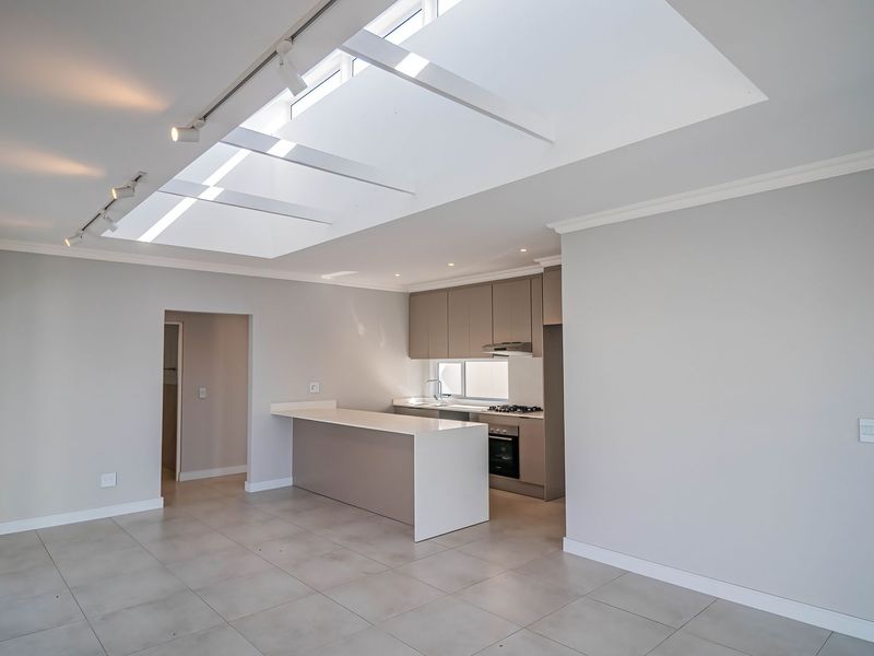 Spacious open-plan living and kitchen area featuring a large skylight, modern cabinetry, stone countertops, and neutral tiled flooring throughout.