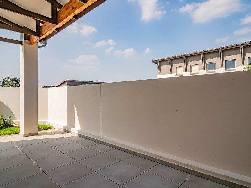 A spacious, tiled outdoor patio area featuring a covered roof structure with exposed timber beams and a private perimeter boundary wall.