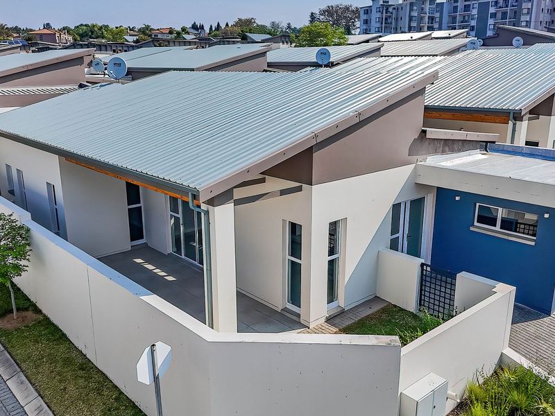 Aerial view of a modern townhouse featuring a corrugated metal roof, paved driveway, and a private covered patio area within a secure complex.