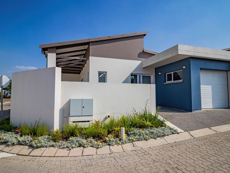 Modern townhouse exterior featuring a paved driveway, single garage, and a clean, contemporary facade with a covered patio area.