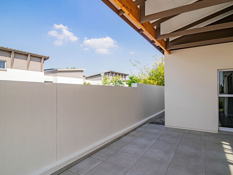 A clean, modern covered patio featuring tiled flooring, exposed timber rafters, and a sliding glass door leading into the townhouse.