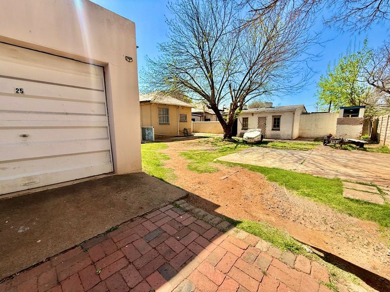 Rear exterior view showing a garage, paved driveway, concrete patio area, and a large garden space with boundary walls.