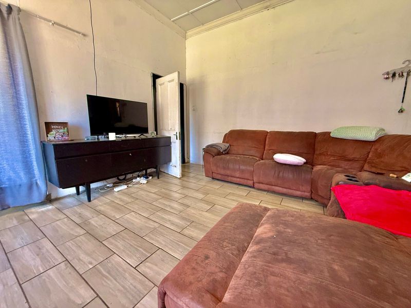 A living room featuring tiled flooring and a panelled ceiling, currently showing signs of wear on the walls and door frames.