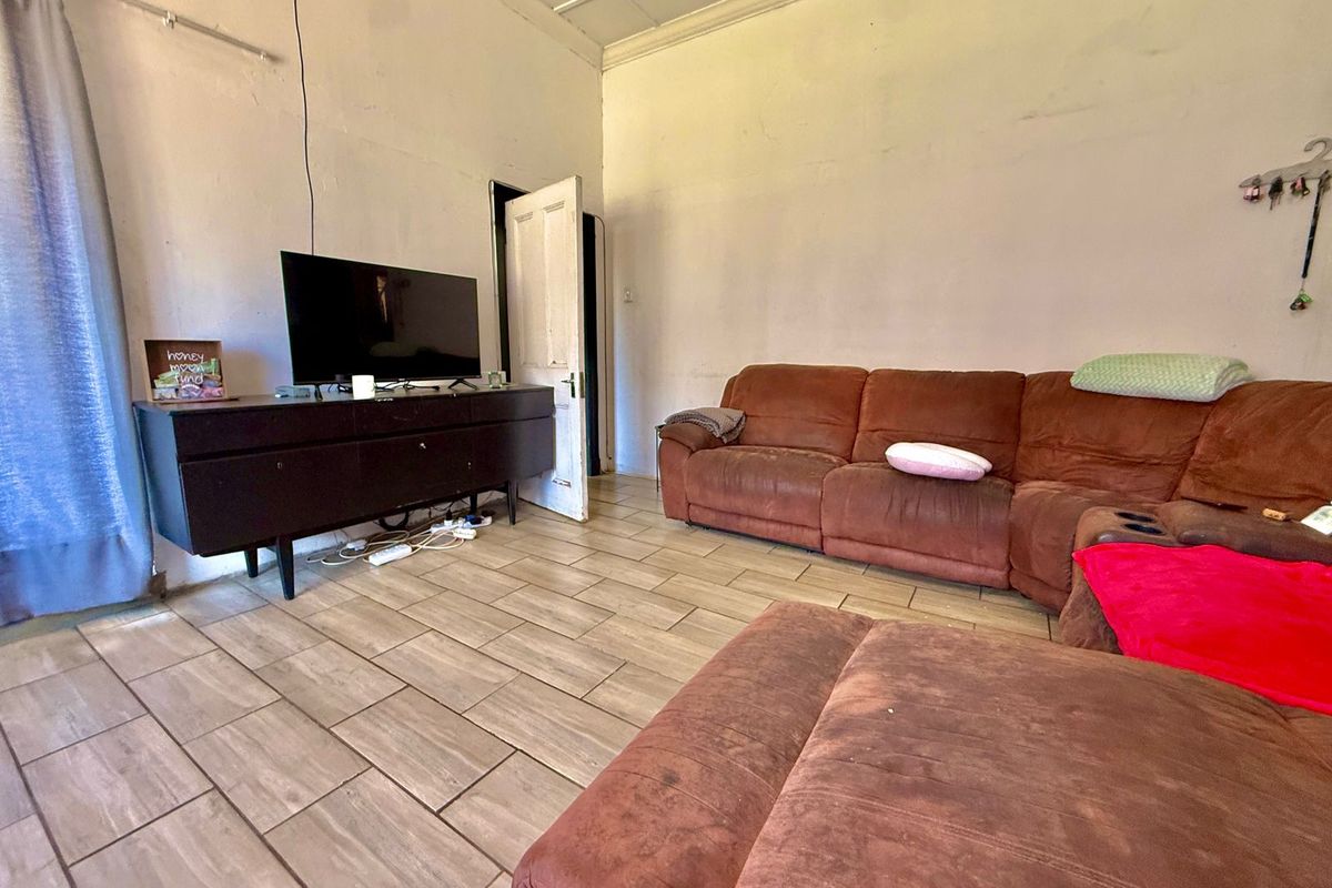 A living room featuring tiled flooring and a panelled ceiling, currently showing signs of wear on the walls and door frames.