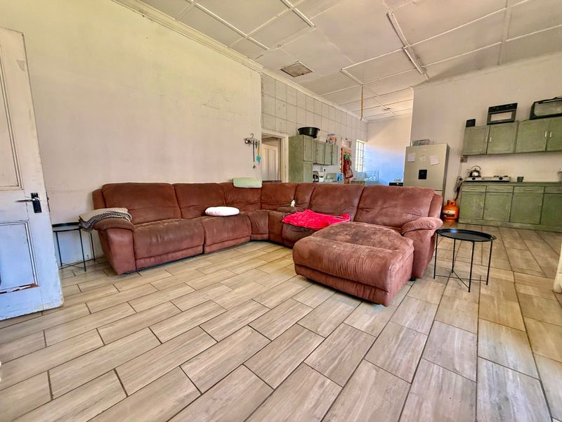 Open-plan living and kitchen area featuring tiled flooring, dated cabinetry, and a tiled splashback, offering potential for modernization and renovation.