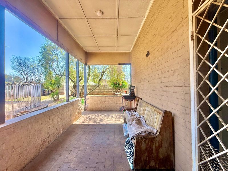 A covered outdoor patio area featuring brick flooring and brick walls, providing a functional space overlooking the rear garden.
