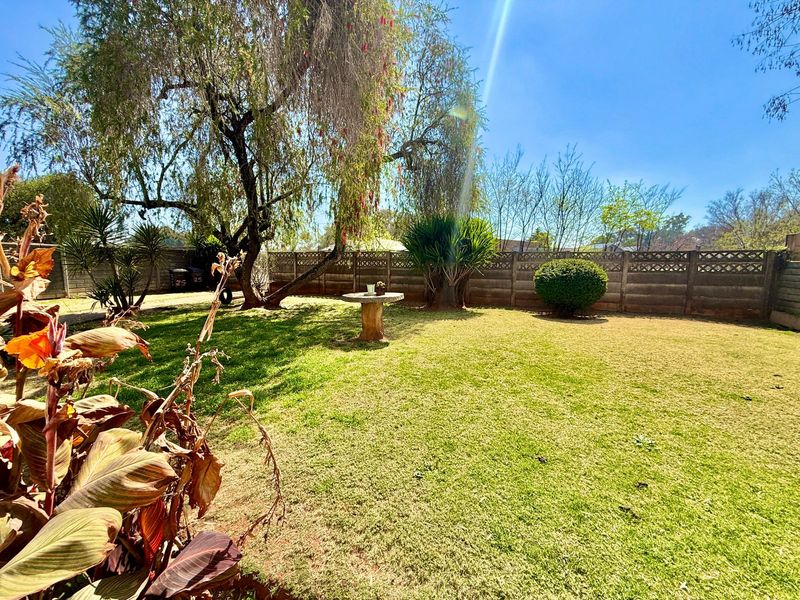 A spacious private garden featuring a well-maintained lawn, mature trees, and a secure precast concrete boundary wall.