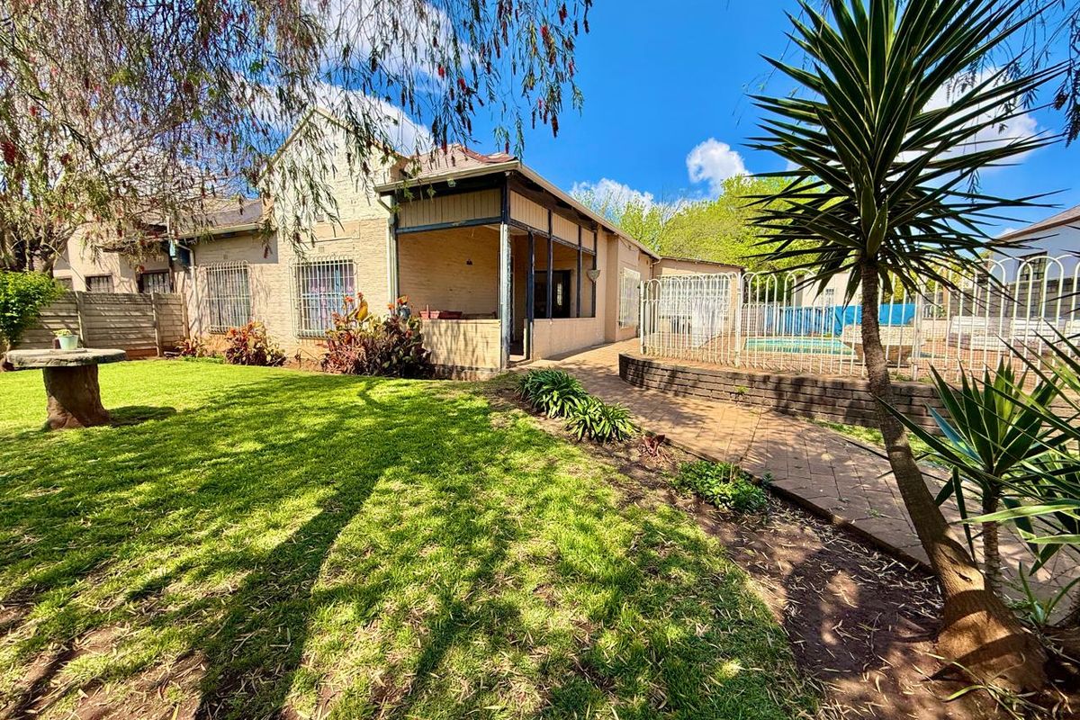 Rear view of the property featuring a covered patio, paved walkway, and a swimming pool set within a landscaped garden.