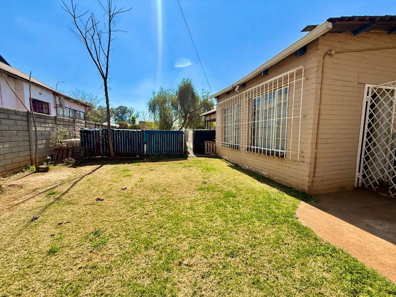 Rear exterior view of the property featuring a private backyard, lawn area, and security bars on the windows.