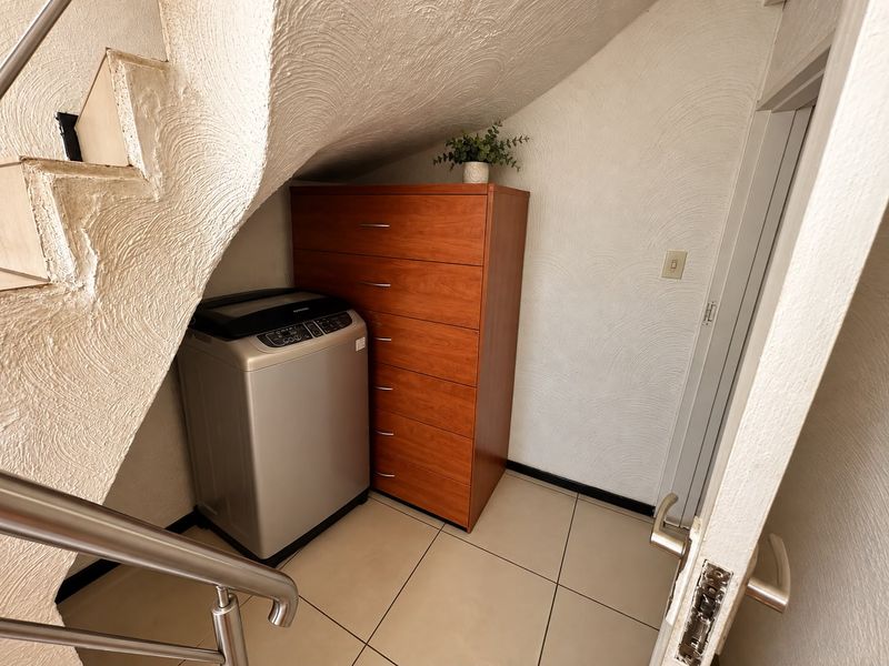 A compact laundry area situated beneath a staircase, featuring tiled flooring and textured walls, providing functional utility space within the home.