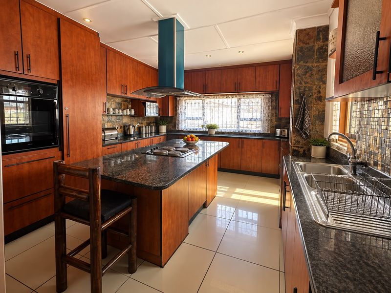Spacious kitchen featuring warm wood cabinetry, granite countertops, a central island with a built-in hob, and modern tiled flooring.