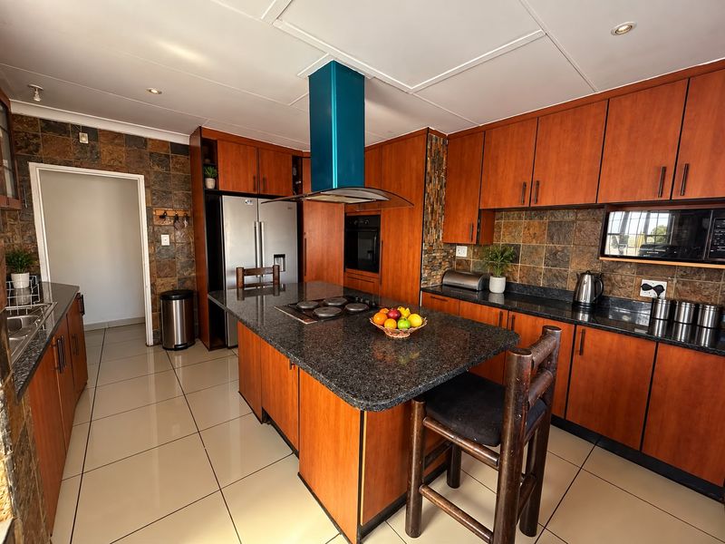 A functional kitchen featuring wooden cabinetry, granite countertops, a central island with a built-in cooktop, and a modern blue extractor fan.