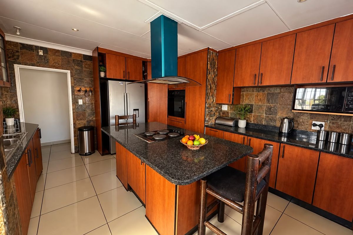 A functional kitchen featuring wooden cabinetry, granite countertops, a central island with a built-in cooktop, and a modern blue extractor fan.