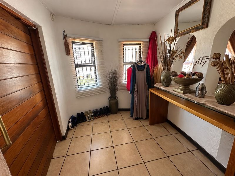 A bright entrance hall featuring tiled flooring, arched wall detailing, and windows fitted with security bars and venetian blinds.
