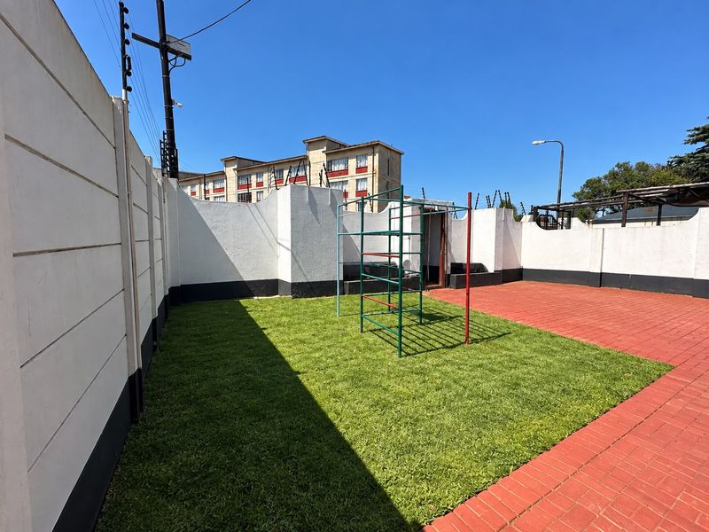 A private backyard featuring a paved patio area, a well-maintained lawn, and secure perimeter walls with electric fencing.