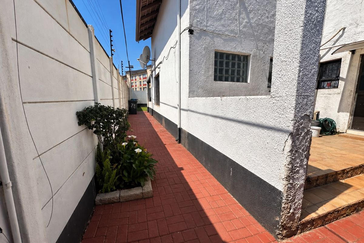 A side exterior walkway featuring red brick paving, a boundary wall with electric fencing, and a tiled patio area.