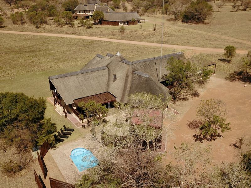 Aerial view of a lodge property featuring a traditional thatch roof, a private swimming pool, and a spacious outdoor patio area set in bushveld.
