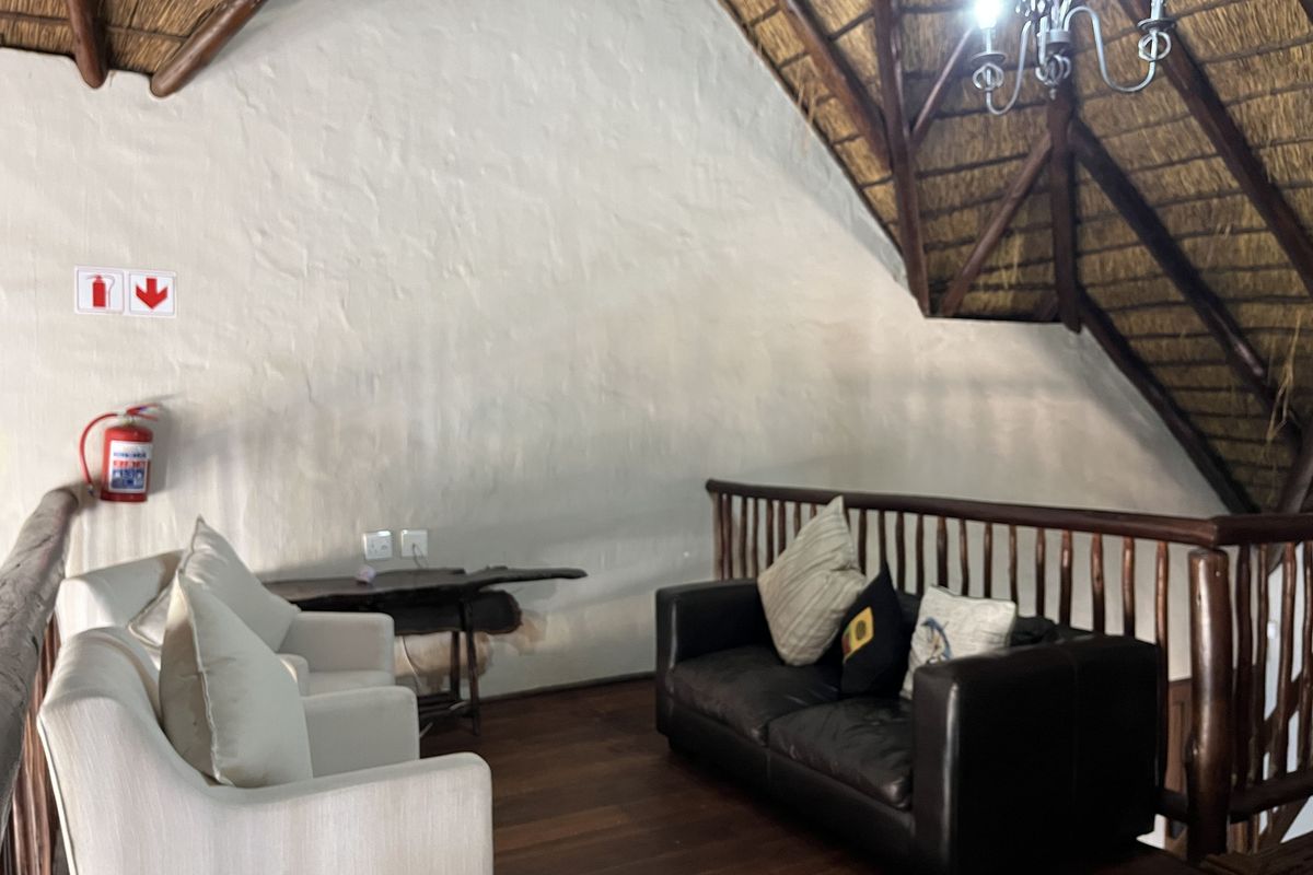 A cozy mezzanine living area featuring a high vaulted thatched roof with exposed timber rafters, hardwood flooring, and a wooden balustrade overlooking the lower level.