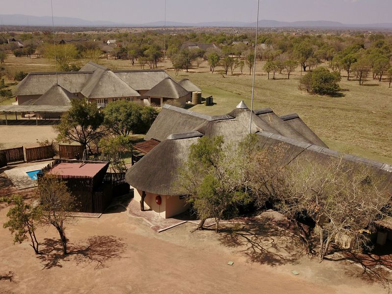 Aerial view of a lodge property featuring multiple thatched-roof buildings, a swimming pool, and expansive surrounding bushveld landscape.