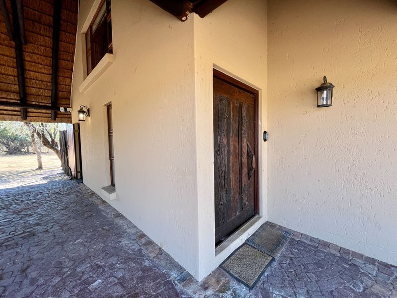 Entrance area of the lodge featuring a rustic timber door, thatched roof overhang, and cobblestone paving.