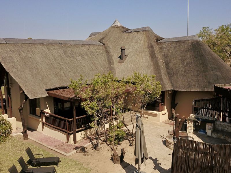Aerial view of the rear lodge exterior featuring a traditional thatched roof, covered patio area, and a stone-paved courtyard with a built-in braai.