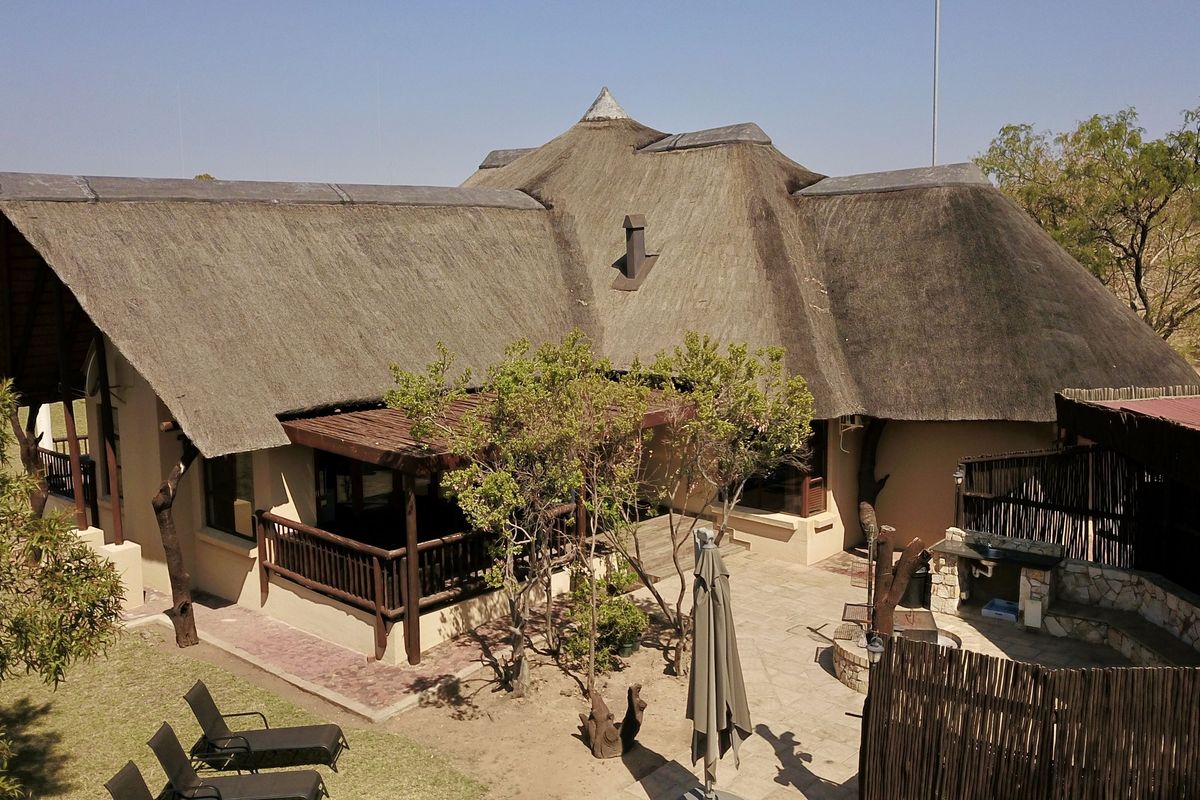 Aerial view of the rear lodge exterior featuring a traditional thatched roof, covered patio area, and a stone-paved courtyard with a built-in braai.