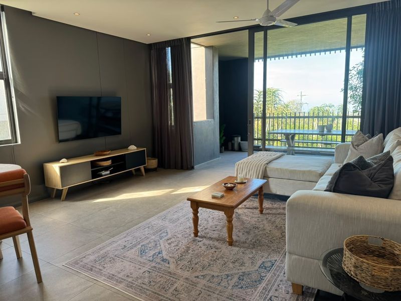 Modern living room featuring large sliding glass doors that open onto a covered balcony, tiled flooring, and recessed ceiling lighting.