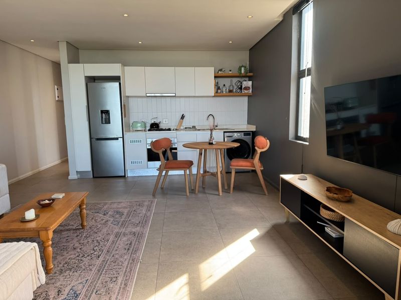 Modern open-plan living area featuring a sleek kitchen with built-in cabinetry, integrated appliances, and neutral tiled flooring throughout the combined space.