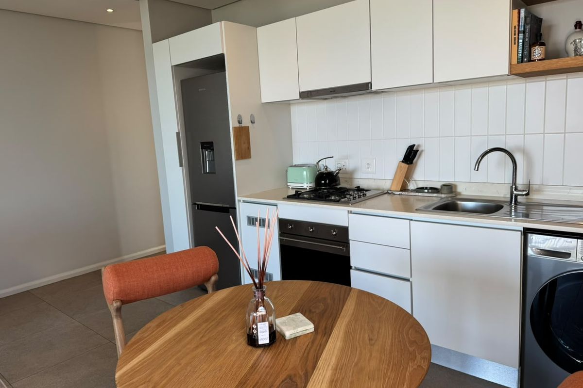 Modern kitchen featuring white cabinetry, gas hob, extractor fan, and integrated appliance space, complemented by a tiled backsplash and stainless steel sink.