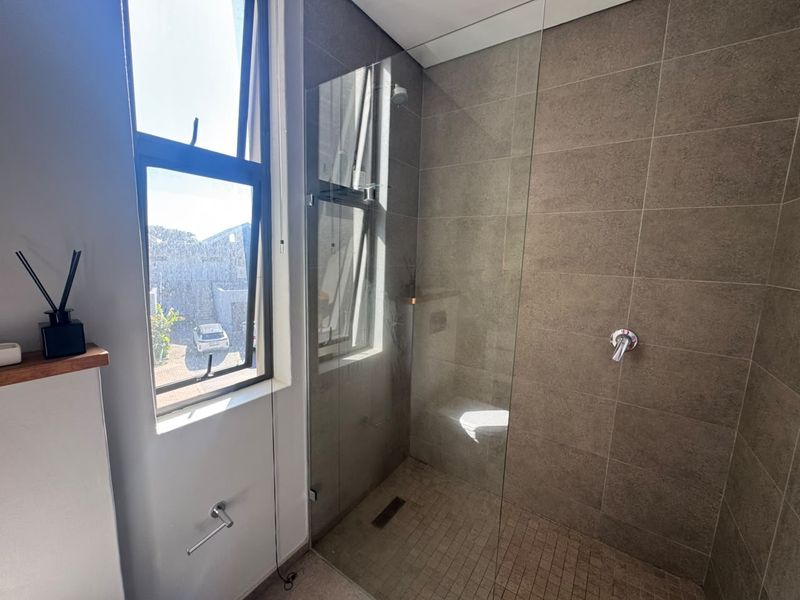 Modern bathroom featuring a walk-in shower with glass screen, neutral wall tiling, and a functional window for natural light.