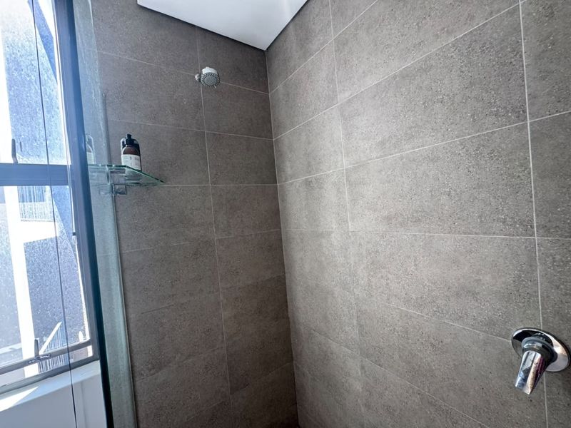 A modern shower enclosure featuring large-format grey wall tiles, a glass screen, and a wall-mounted shower head with integrated mixer tap.